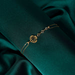 Gold-tone double-chain bracelet with an openwork seashell charm and three clear faceted beads on dark teal fabric.