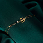 Gold-tone double-chain bracelet with an openwork four-leaf clover and three clear faceted accents on dark teal fabric.