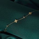 Gold-toned chain bracelet with flat clover shapes, circular cutouts and faceted beads, laid diagonally on dark green fabric.