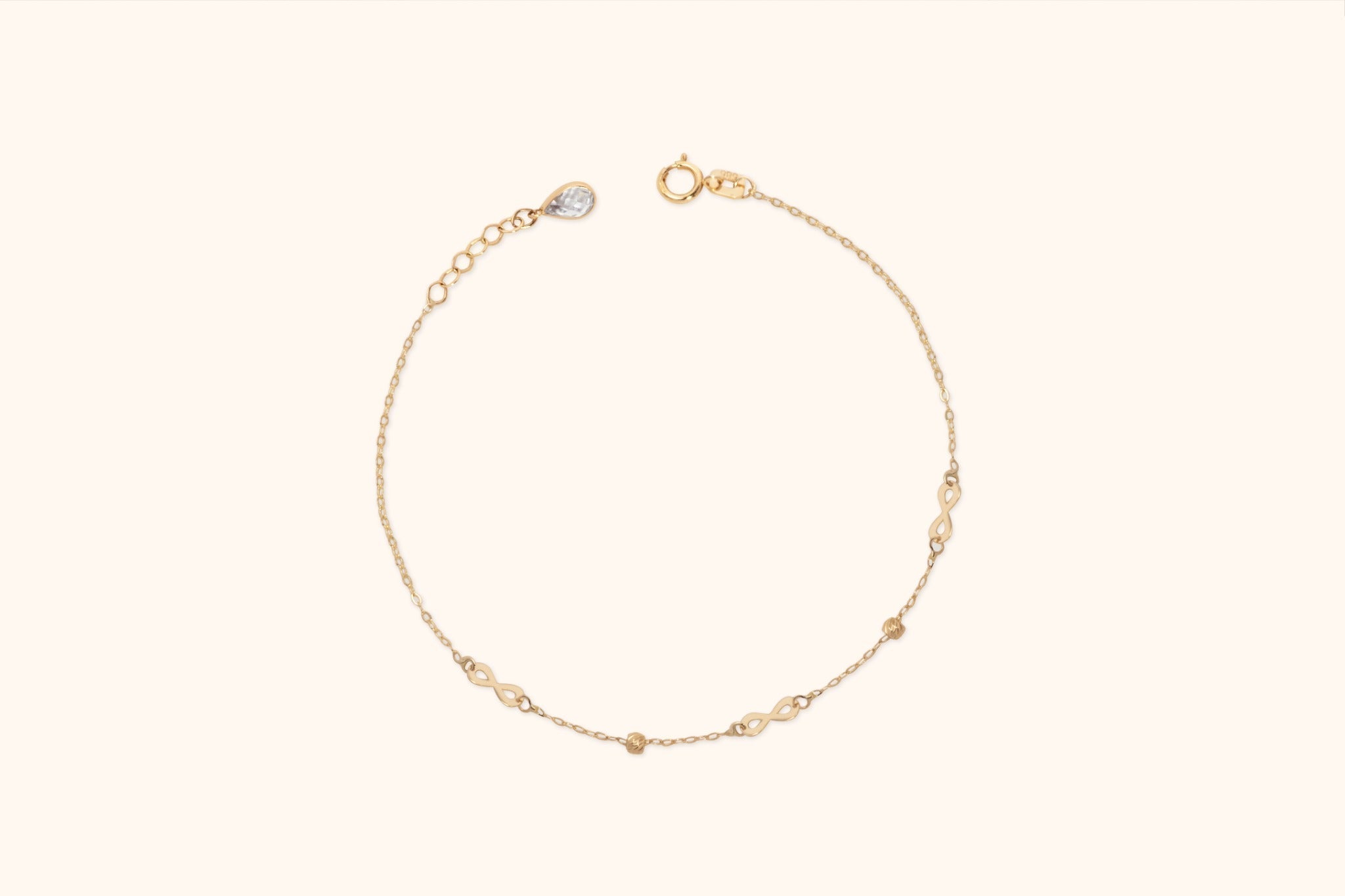 Gold-colored fine chain bracelet with three infinity links, two small beads, a round clasp and an extender with a teardrop charm.