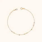 Gold-colored fine chain bracelet with three infinity links, two small beads, a round clasp and an extender with a teardrop charm.