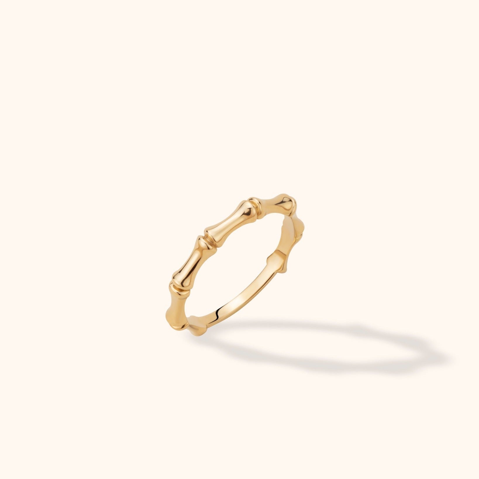 Polished gold-colored ring with bamboo-like segments and raised joints, tilted against a cream background with a soft shadow.