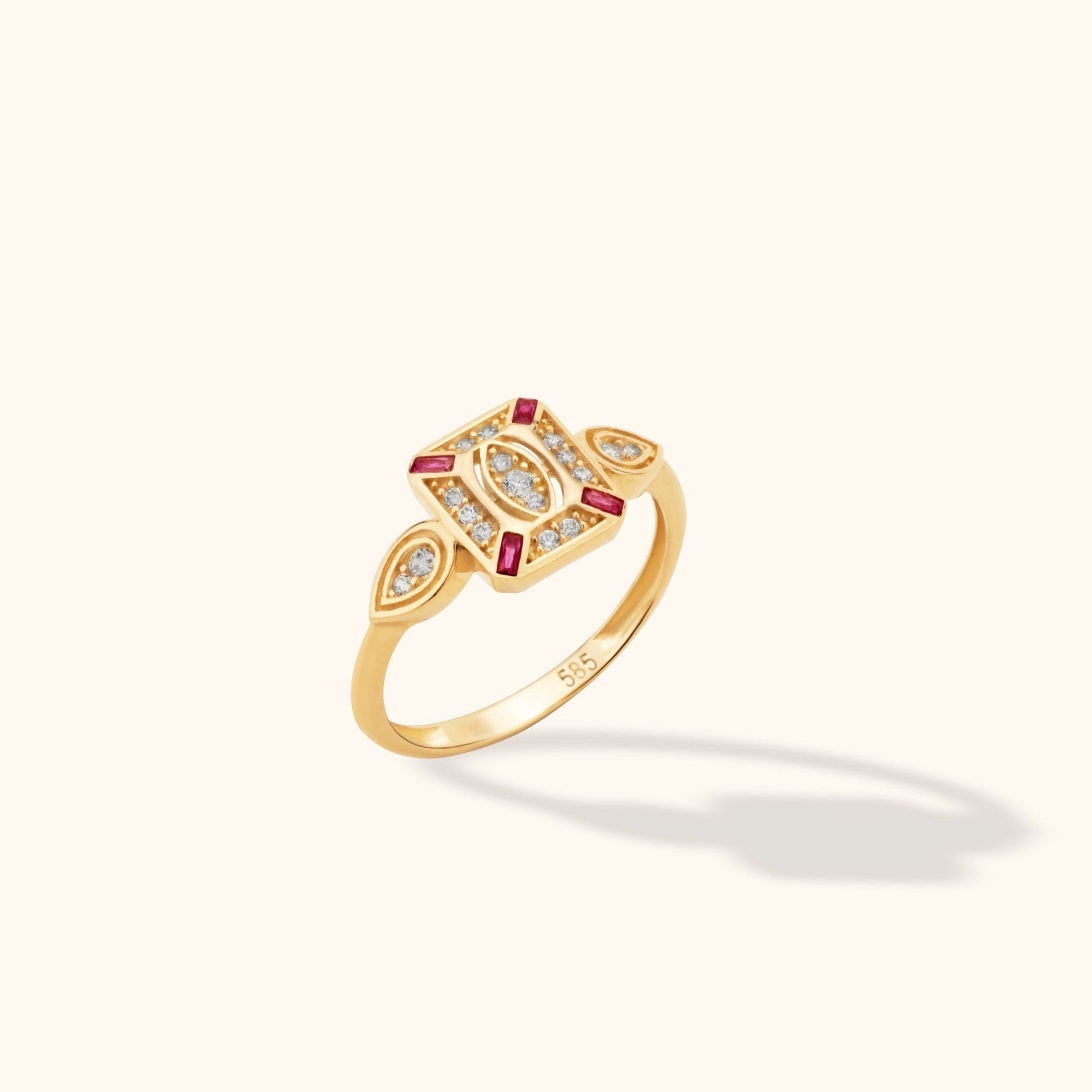 Gold-tone ring with a geometric face, rectangular pink-red stones, round clear stones and teardrop-shaped side details.