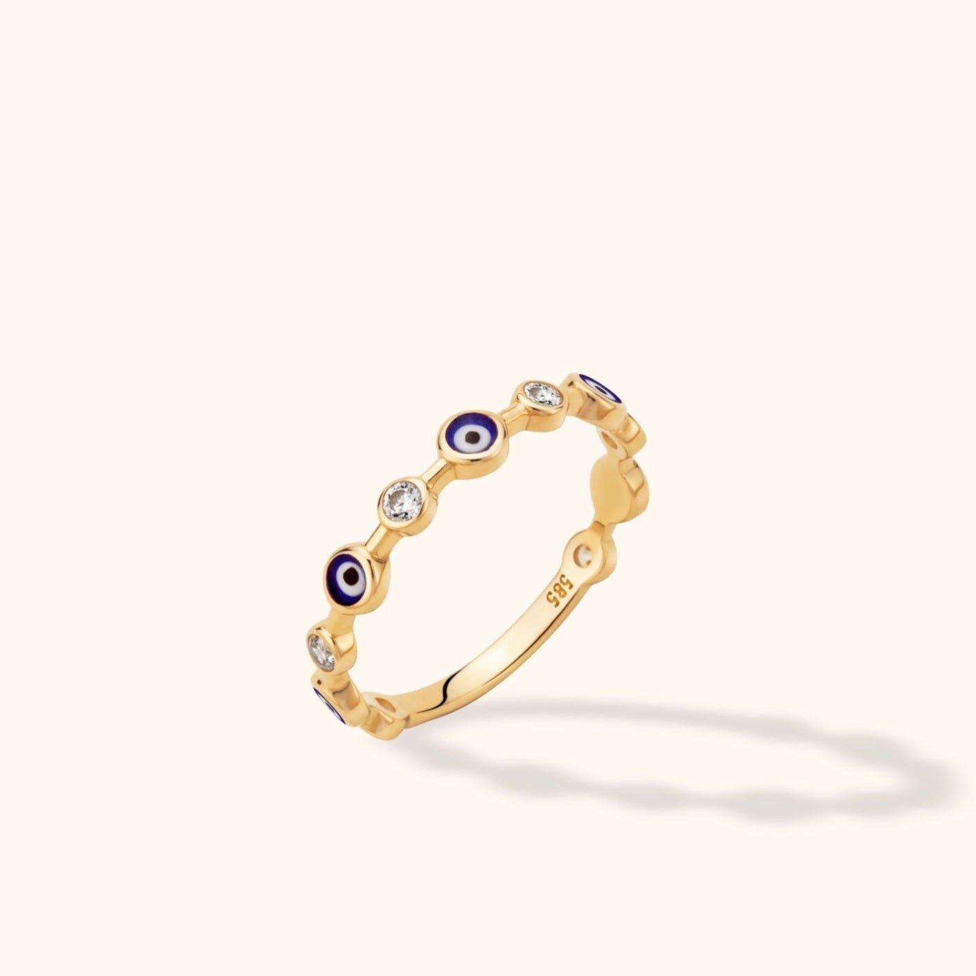 Gold-colored ring with alternating blue-and-white eye motifs and clear round accents, shown tilted on a pale background.