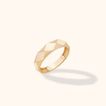 Gold-toned ring with angular geometric facets and a visible 585 stamp inside, tilted against a cream background.