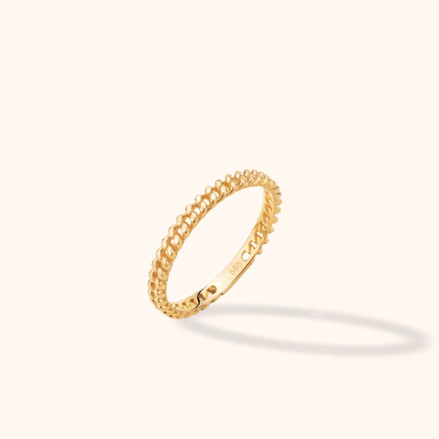Slim gold-toned ring with an interlocking braided pattern, tilted upright on a cream background with a soft shadow.