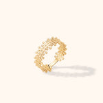 Gold-colored ring with an open grid pattern and rounded bar ends, shown tilted on a cream background with a soft shadow.