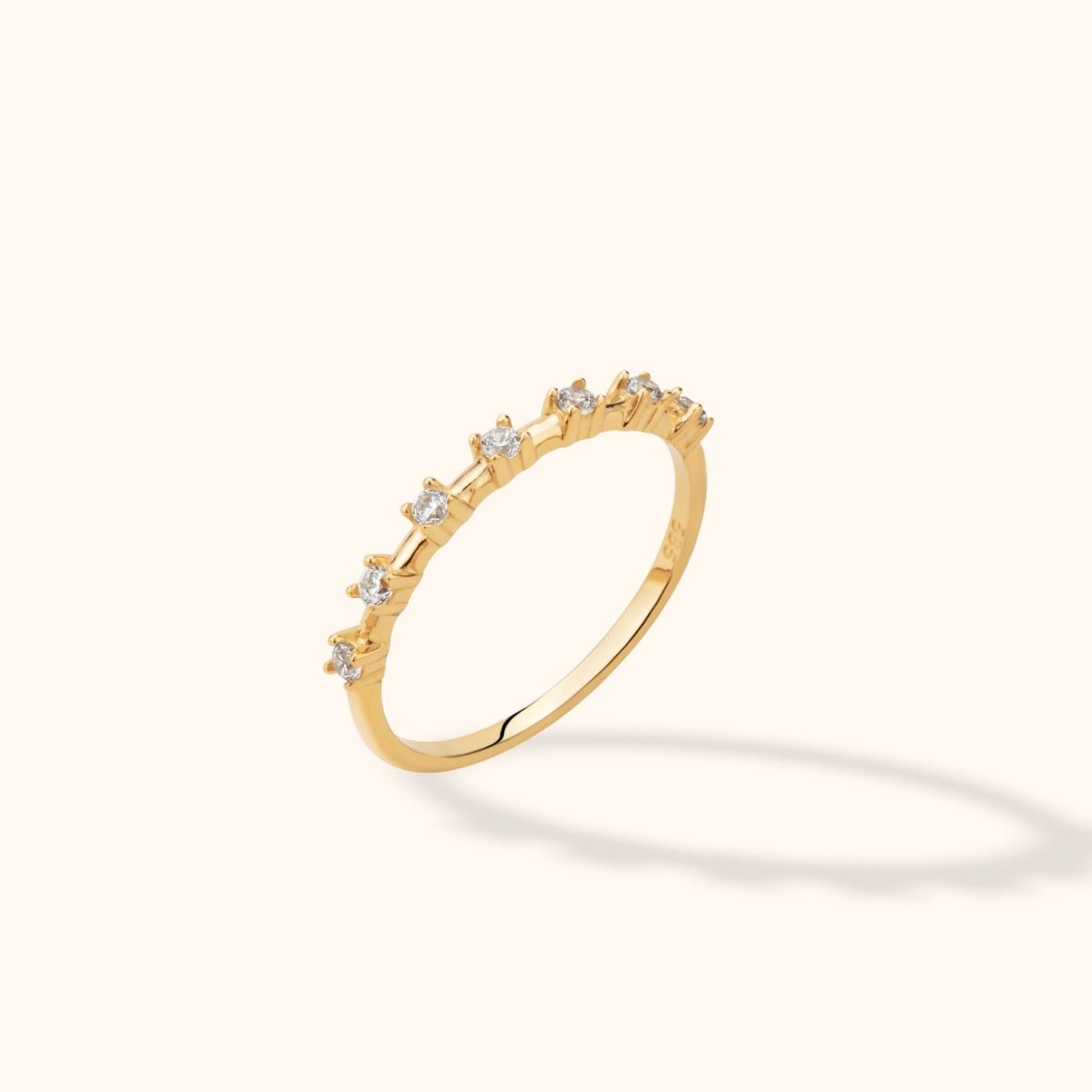Slim gold-toned ring with spaced round clear stones in raised prong settings, shown tilted on a pale background.
