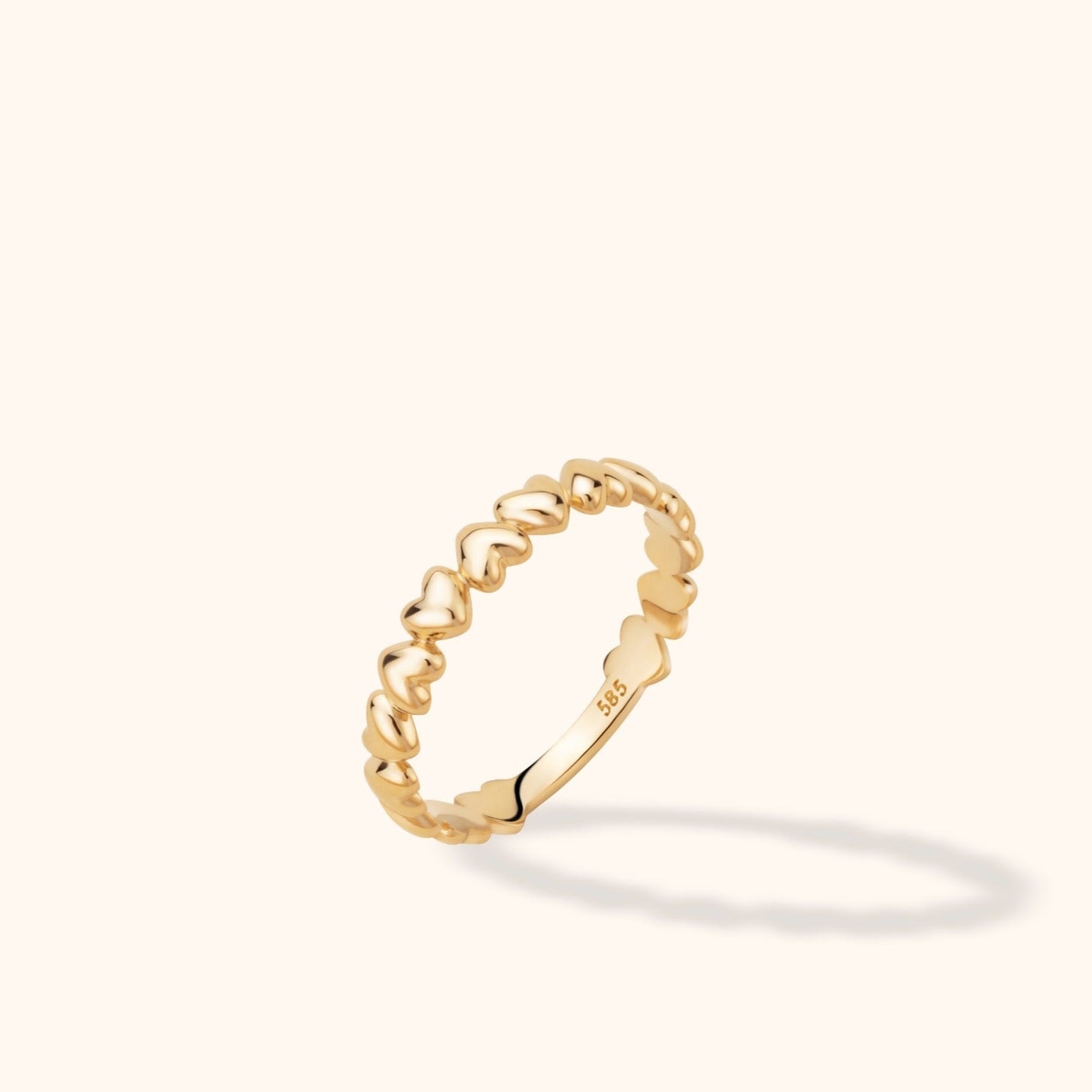 Polished gold-tone ring with a repeating heart design and a visible 585 stamp, tilted against a cream background.