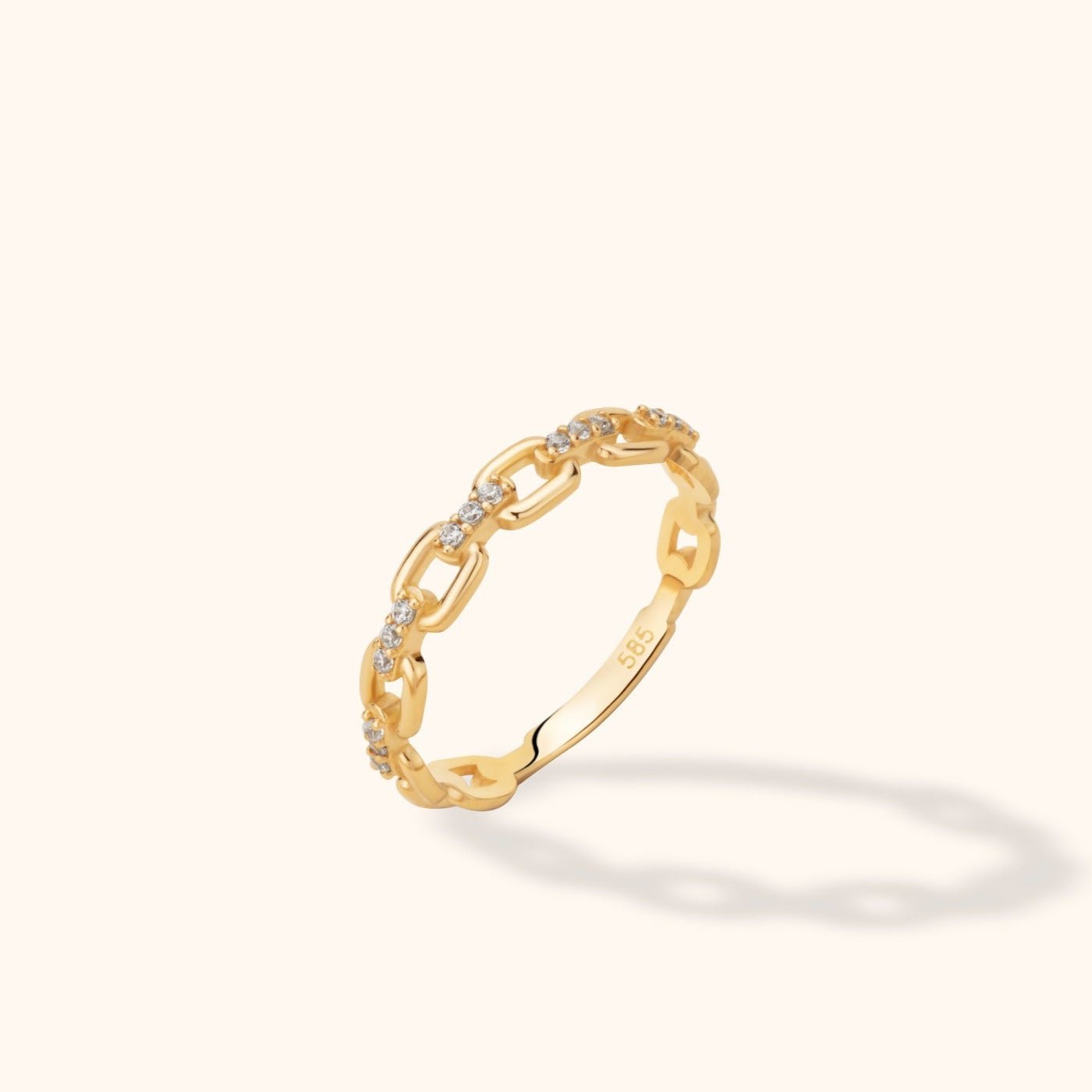 Gold-toned ring with open rectangular chain links and small clear accents, tilted upright on a cream background.
