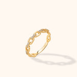 Gold-toned ring with open rectangular chain links and small clear accents, tilted upright on a cream background.