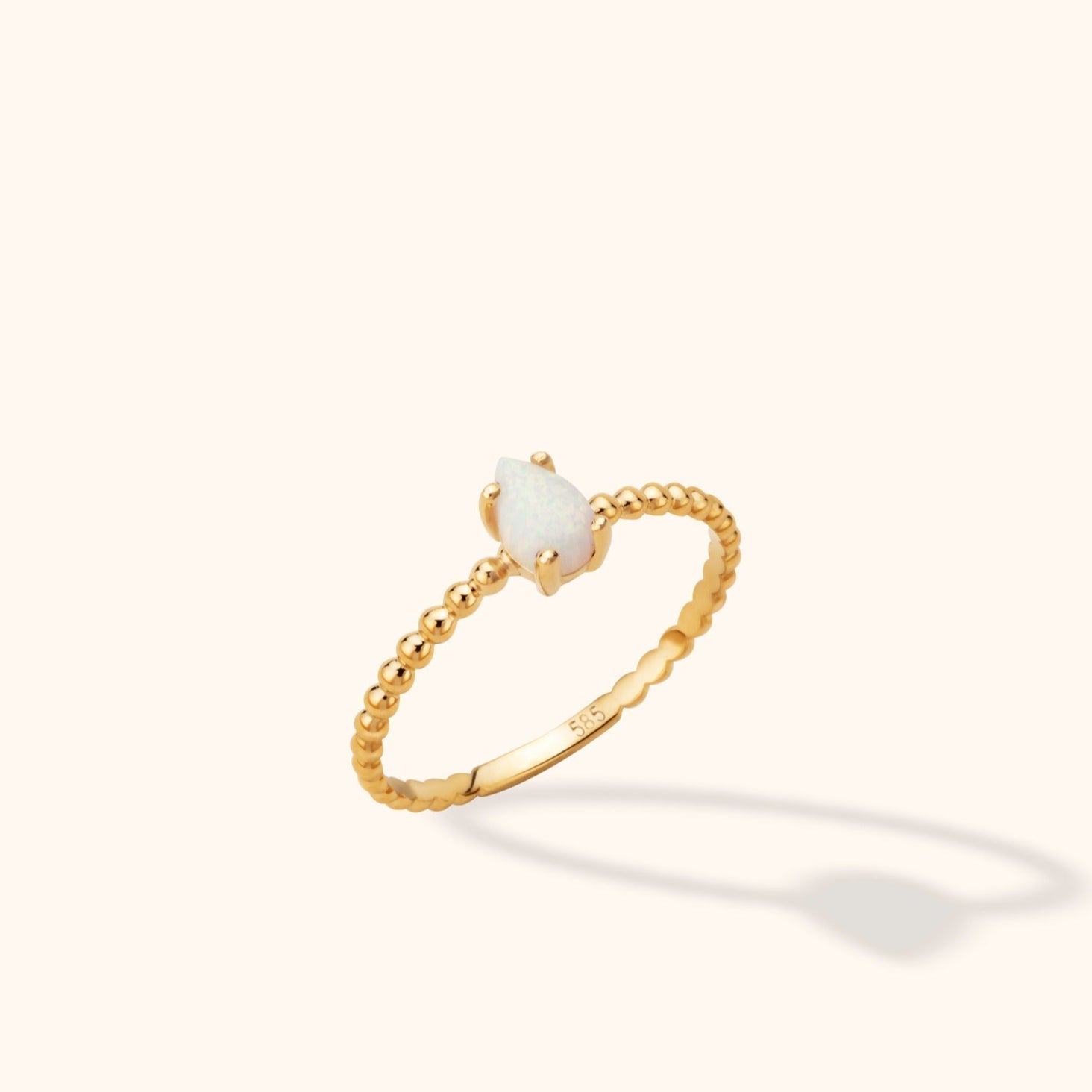 Gold-toned ring with a slim beaded band and a milky white teardrop-shaped center held in prongs, shown at an angle.
