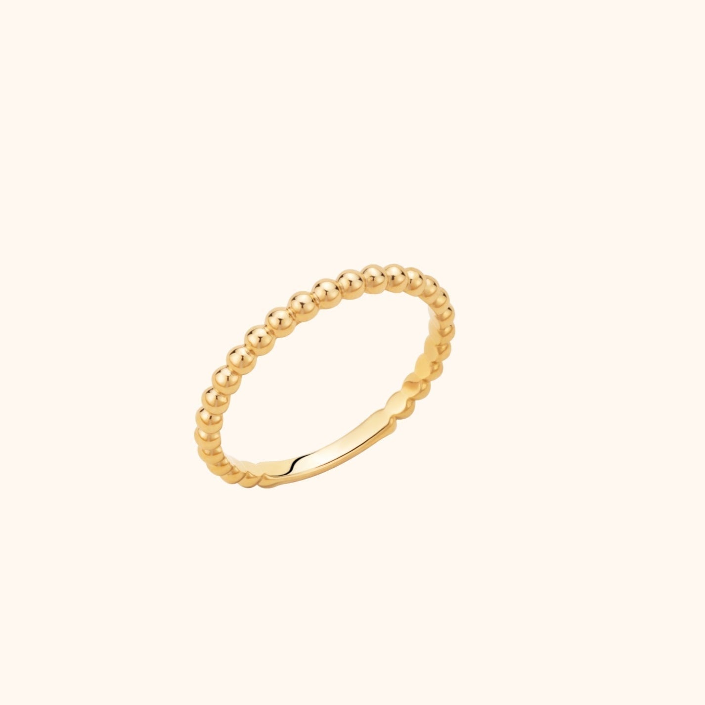 Slim gold-colored ring with rounded bead-like detailing and a smooth lower section, angled against a pale cream background.
