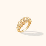Gold-toned ring with rounded, polished ribs alternating with rows of small clear stones, shown at an angle on a cream background.