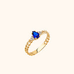 Gold-toned chain-link ring with a pear-shaped blue center stone and small clear stones on either side, shown at an angle.