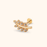 Gold-toned leaf sprig stud earring with clear round accents, a curved stem and a flat disc back on a cream background.