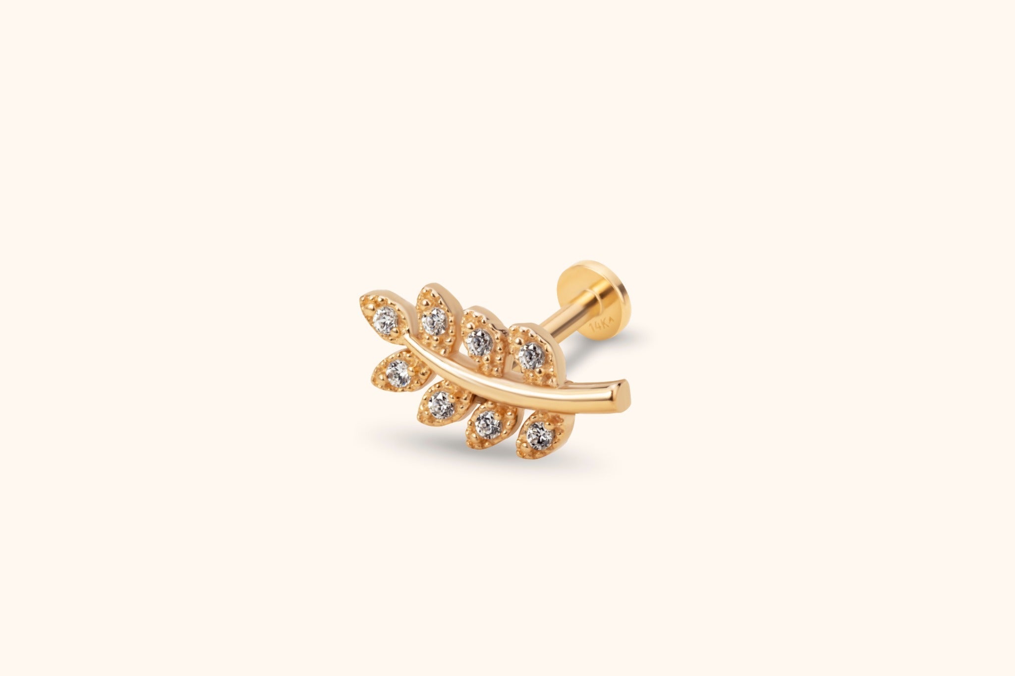 Gold-toned leaf sprig stud earring with clear round accents, a curved stem and a flat disc back on a cream background.