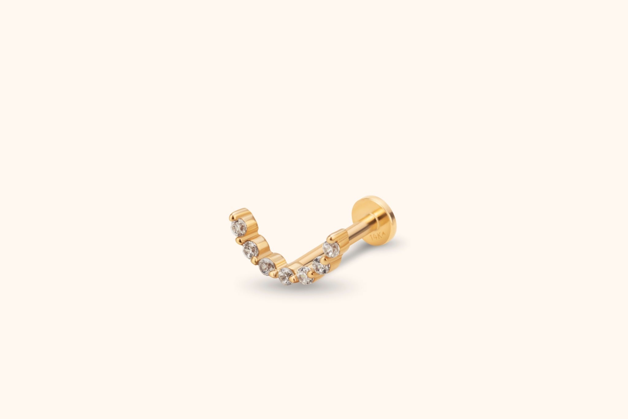 Gold-toned piercing stud with a curved row of clear round stones, a straight post and a flat disc back on a cream background.