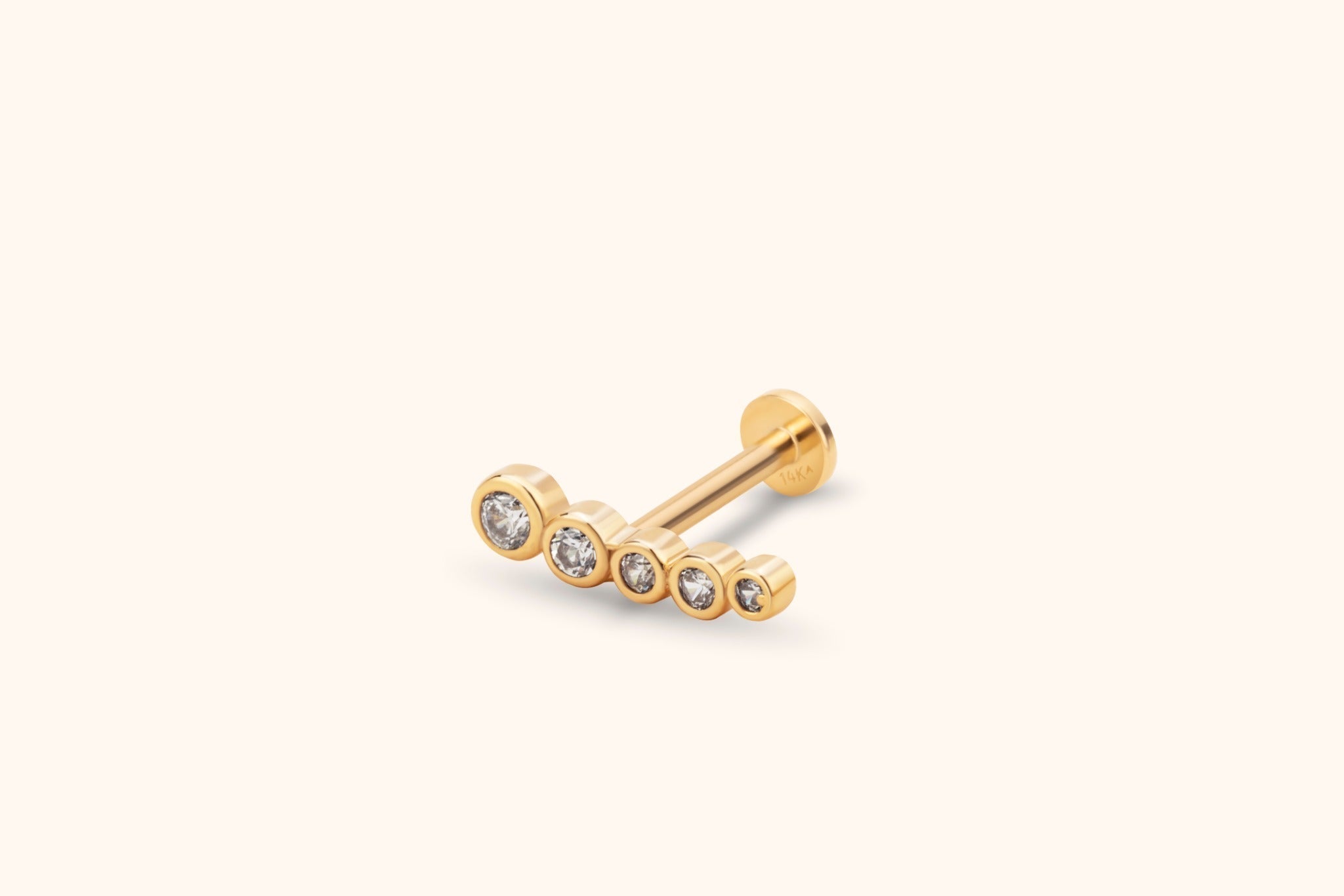 Gold-toned flat-back stud with five clear round accents in bezel settings, arranged in a gently curved row from large to small.