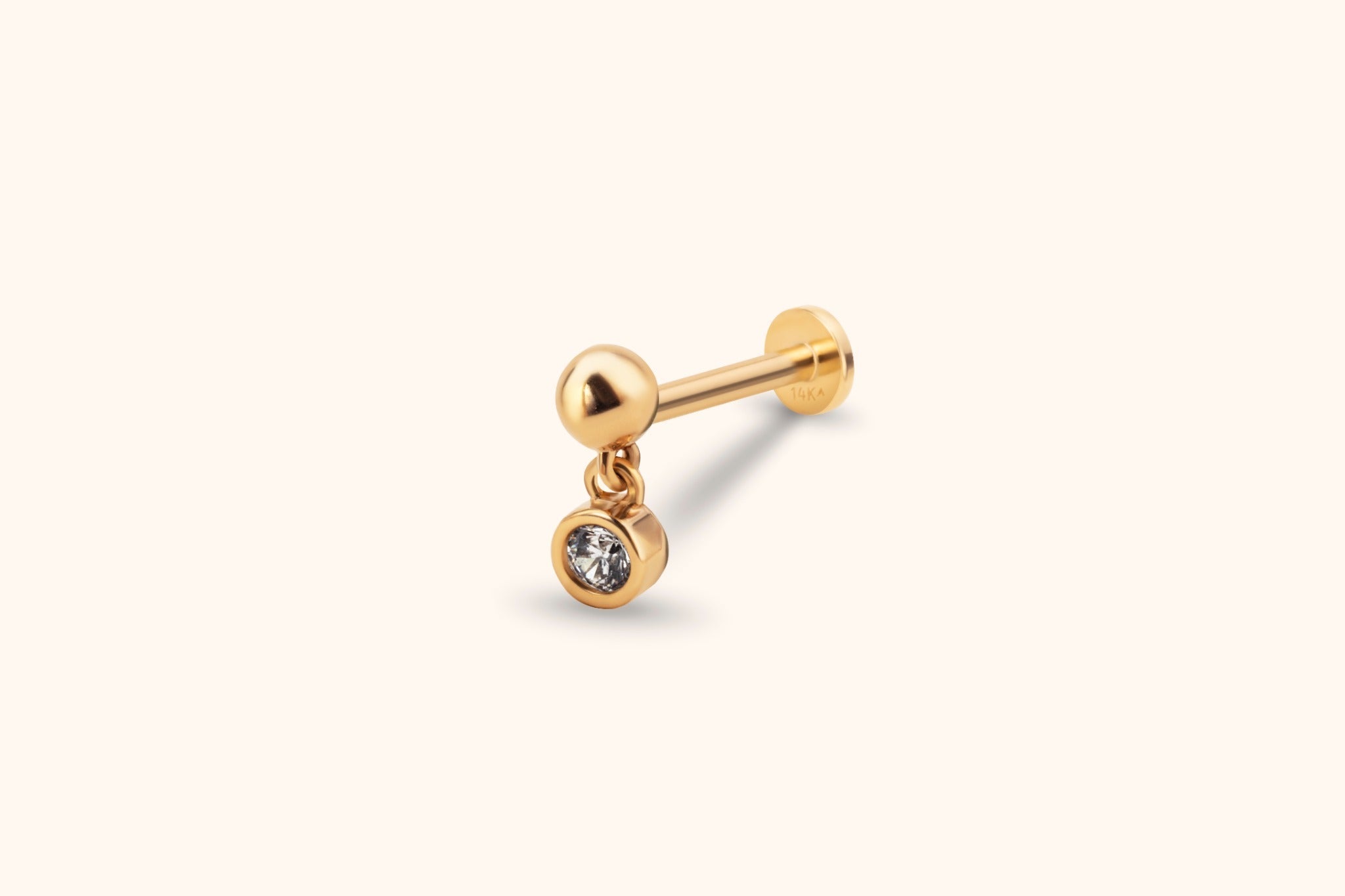 Gold-toned piercing stud with a polished ball, flat disc back and dangling round clear stone in a smooth bezel setting.