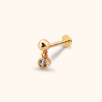 Gold-toned piercing stud with a polished ball, flat disc back and dangling round clear stone in a smooth bezel setting.