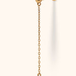 Gold-tone piercing stud with a ball front, flat disc back and long dangling chain ending in a round, bezel-set clear stone.