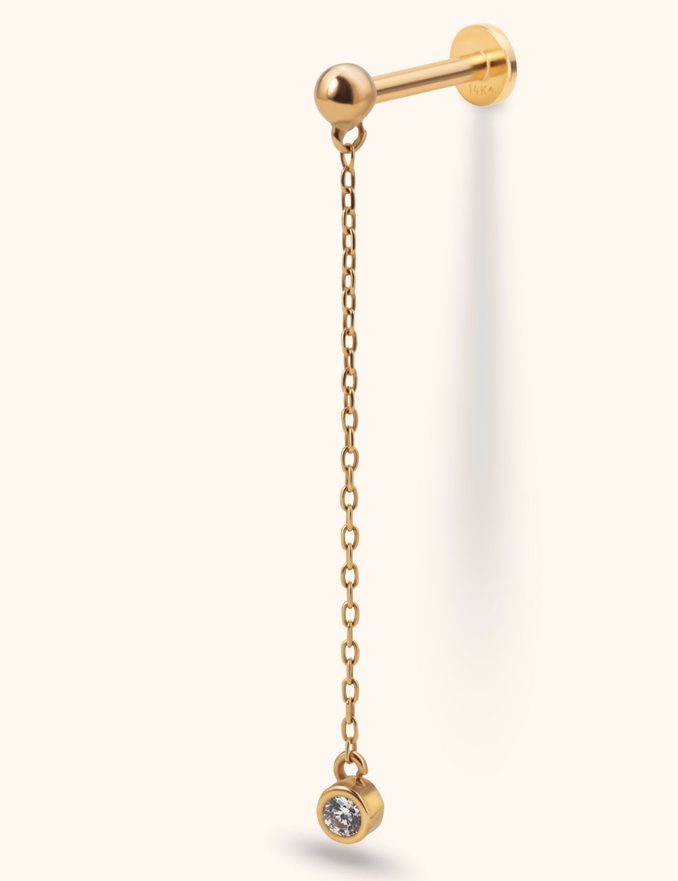 Gold-tone piercing stud with a ball front, flat disc back and long dangling chain ending in a round, bezel-set clear stone.