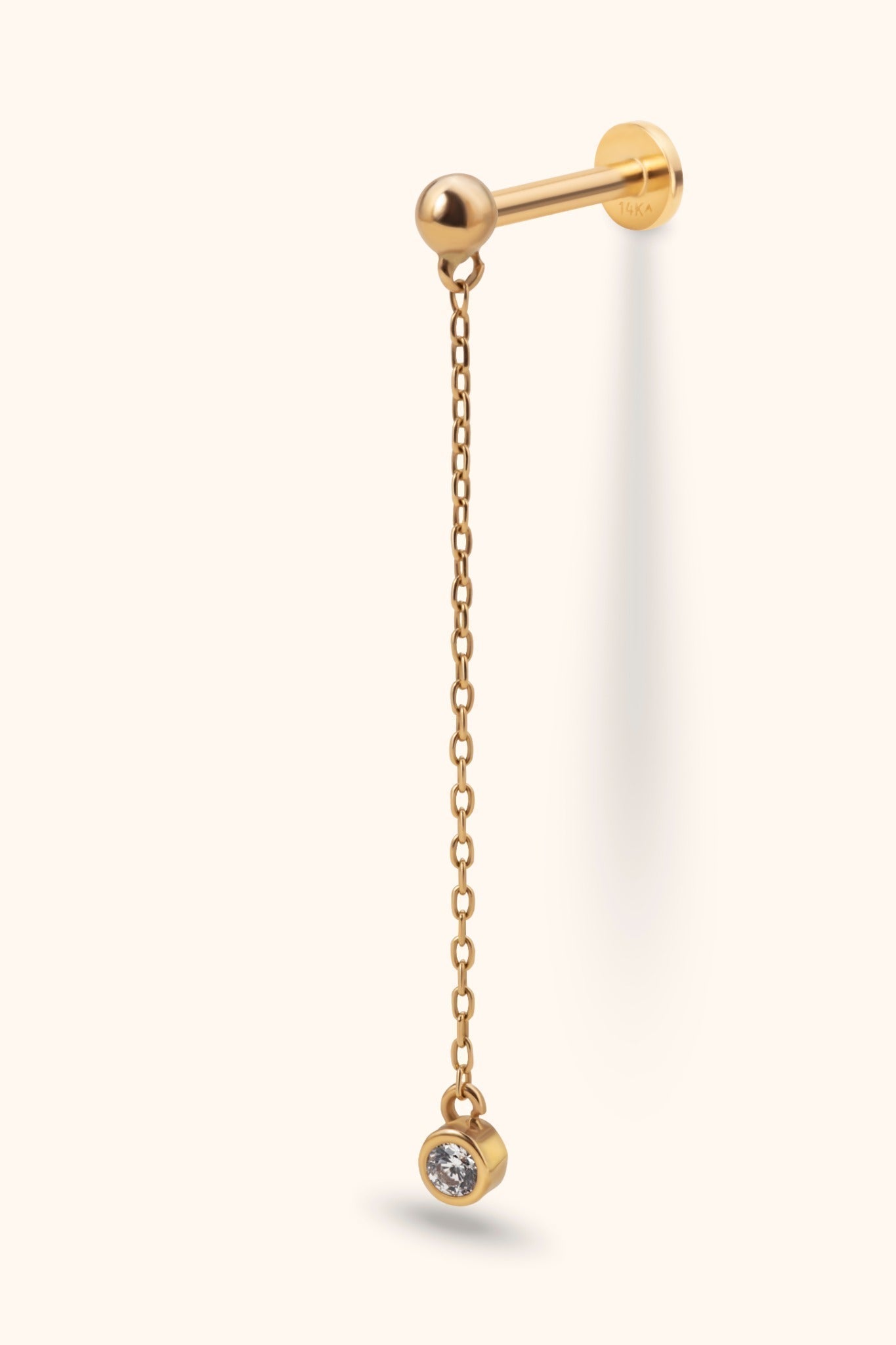 Gold-tone piercing stud with a ball front, flat disc back and long dangling chain ending in a round, bezel-set clear stone.