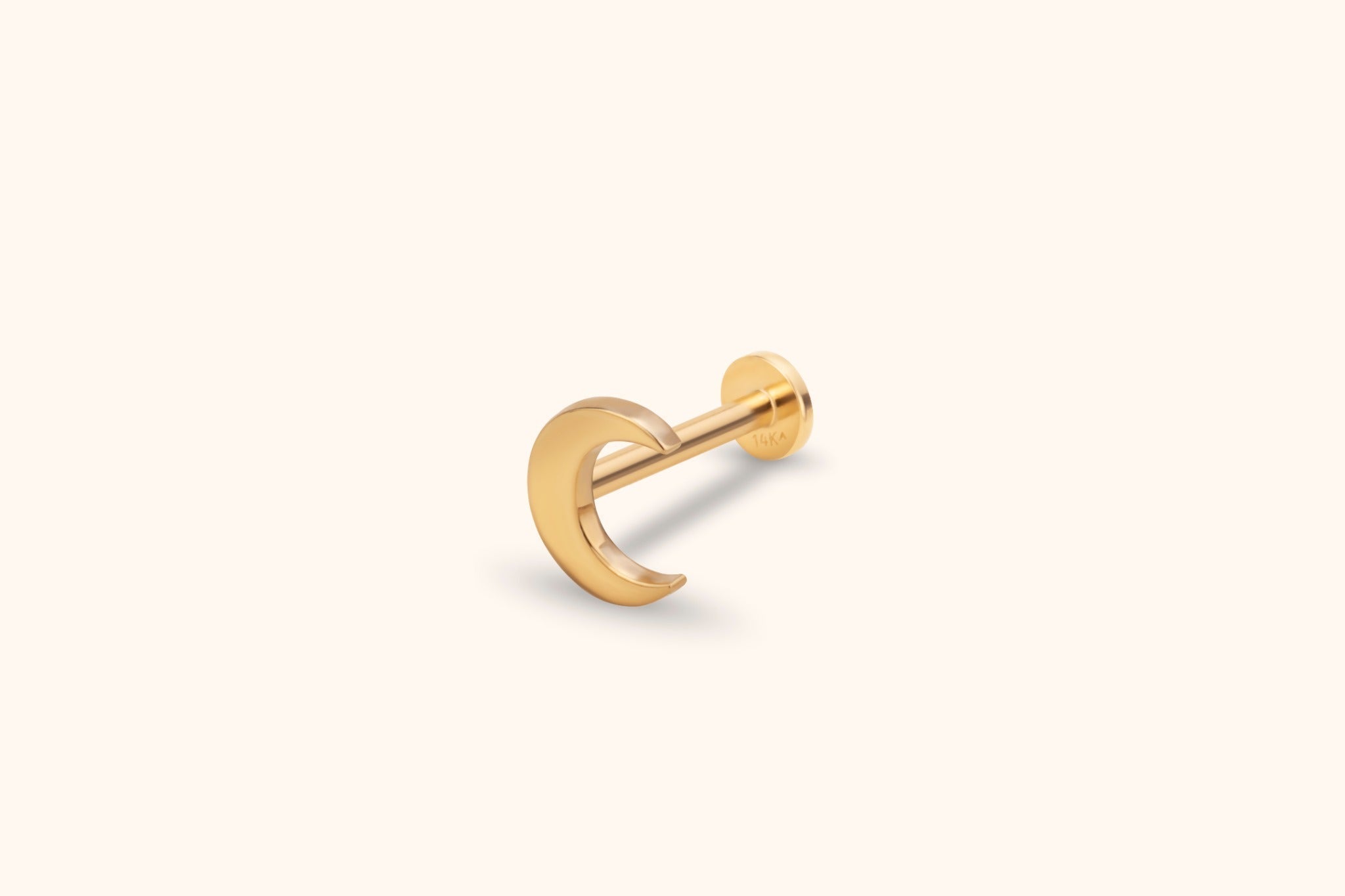 Gold-toned crescent moon piercing stud with a straight post and round flat back, shown at an angle on a cream background.