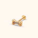 Gold-colored dog bone stud with three round clear stones, a straight post and flat circular back on a cream background.