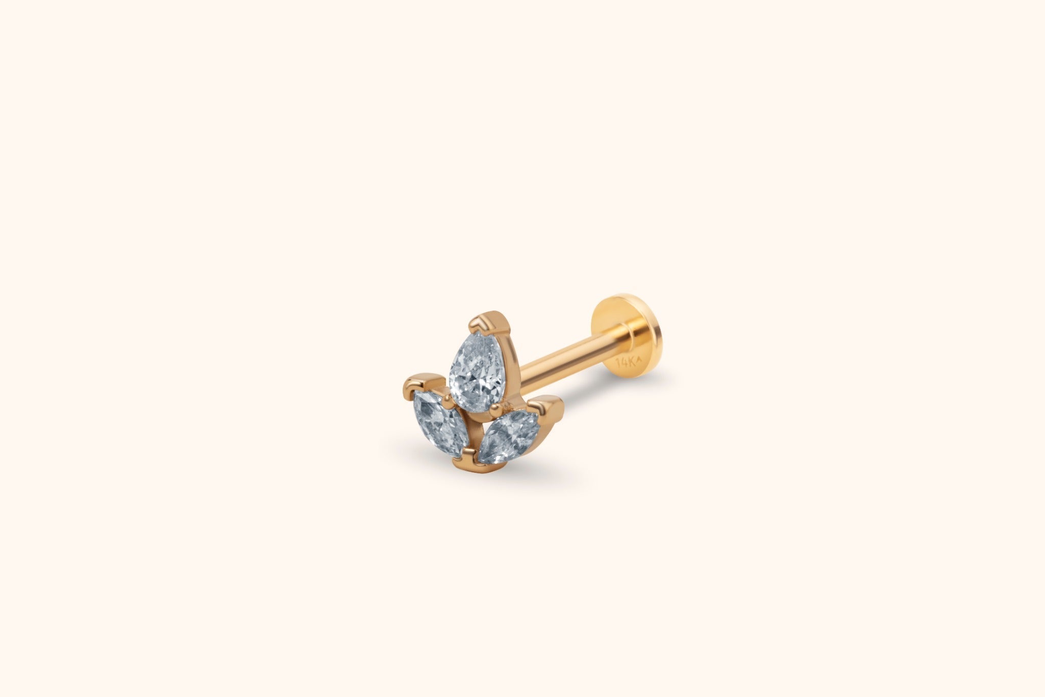 Gold-toned flat-back stud with a cluster of one pear-shaped and two marquise-shaped clear stones on a cream background.