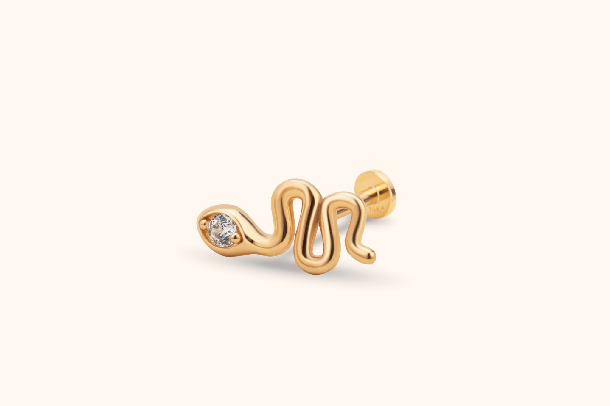 Gold-toned snake stud earring with a wavy body, clear faceted detail at the head, and a round flat back on a cream background.