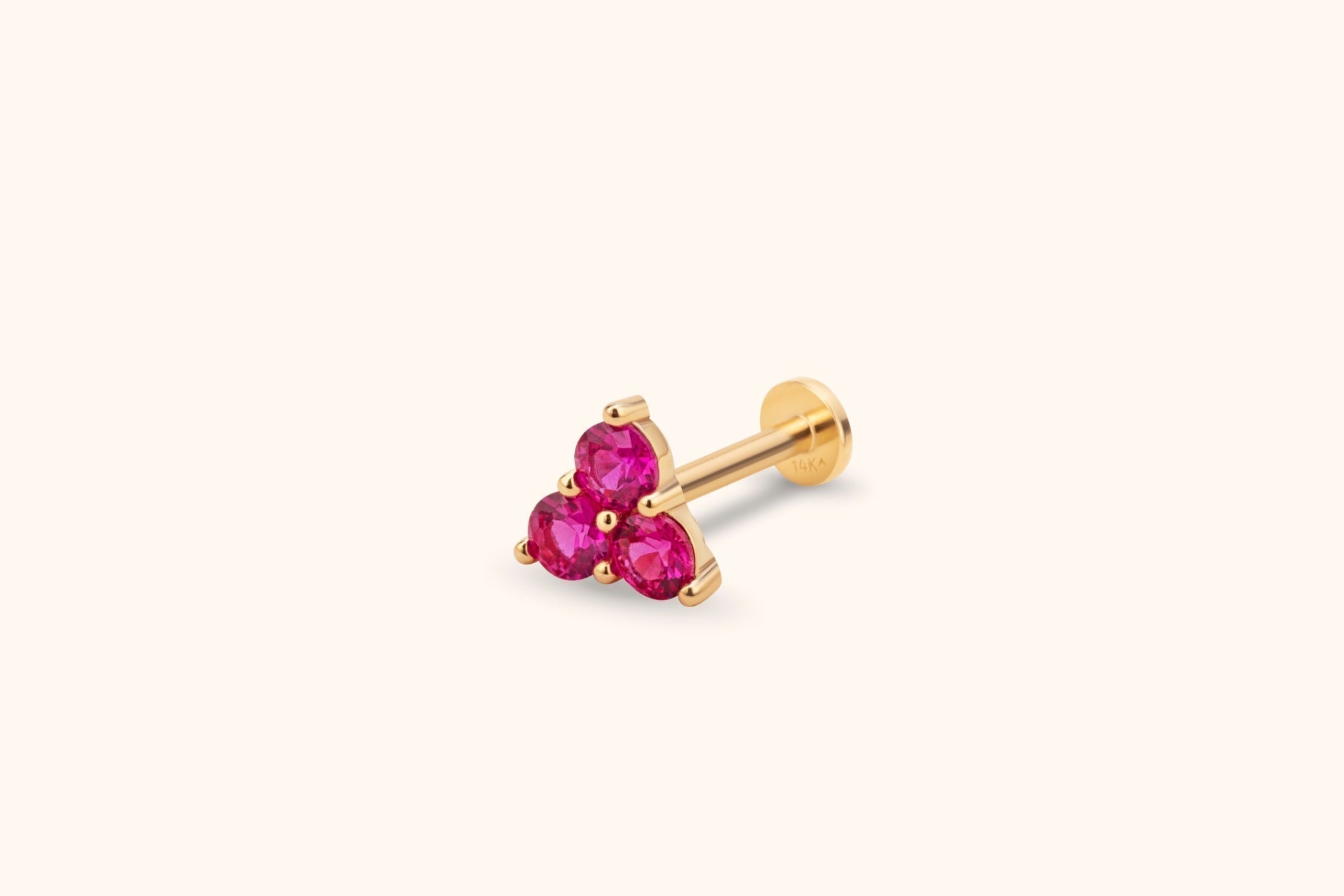 Gold-colored flat-back stud with three round, faceted pink stones in a triangular cluster on a cream background.