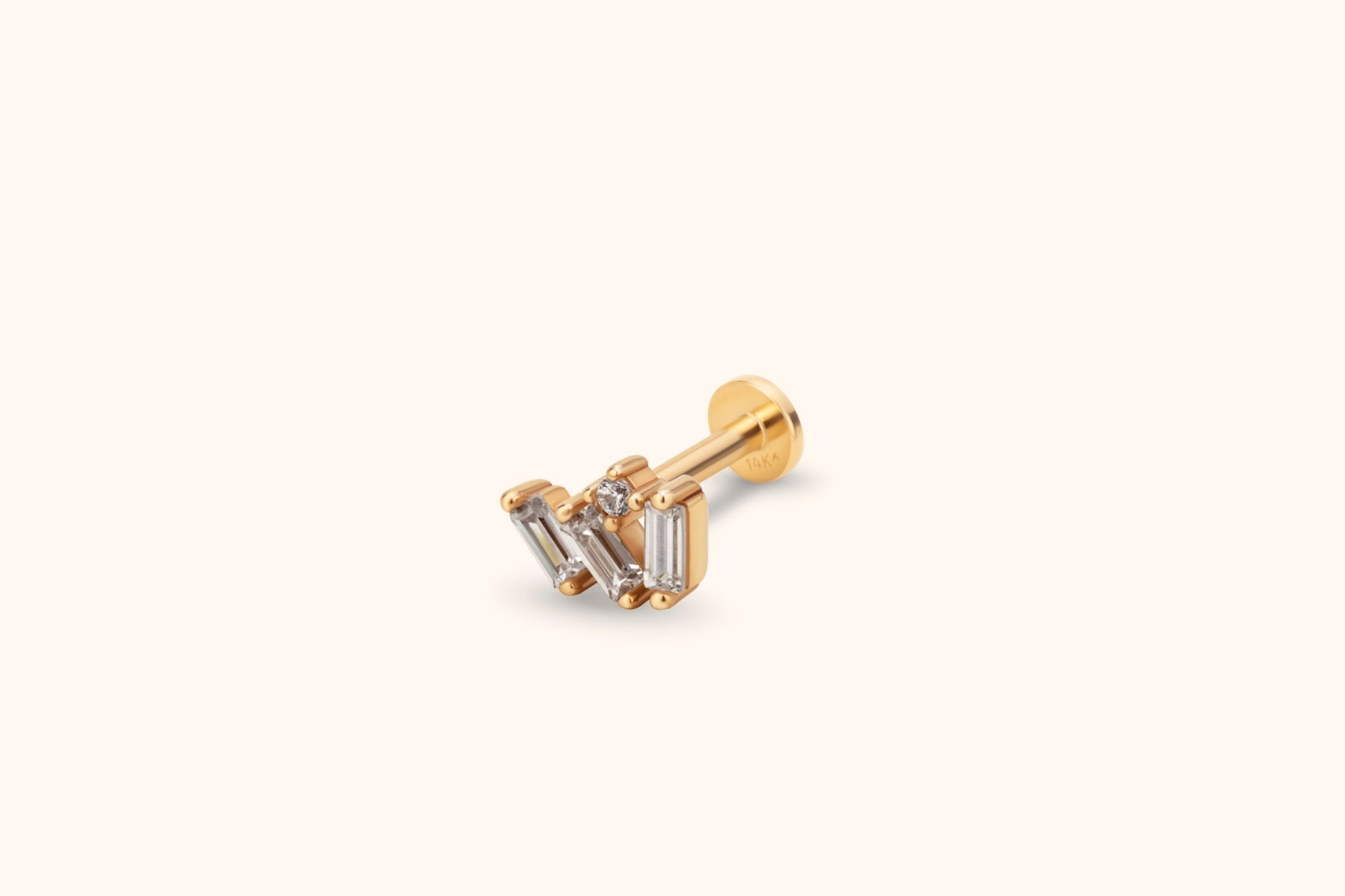 Gold-toned flat-back stud with three clear rectangular stones and a small round accent in a clustered setting on a cream background.