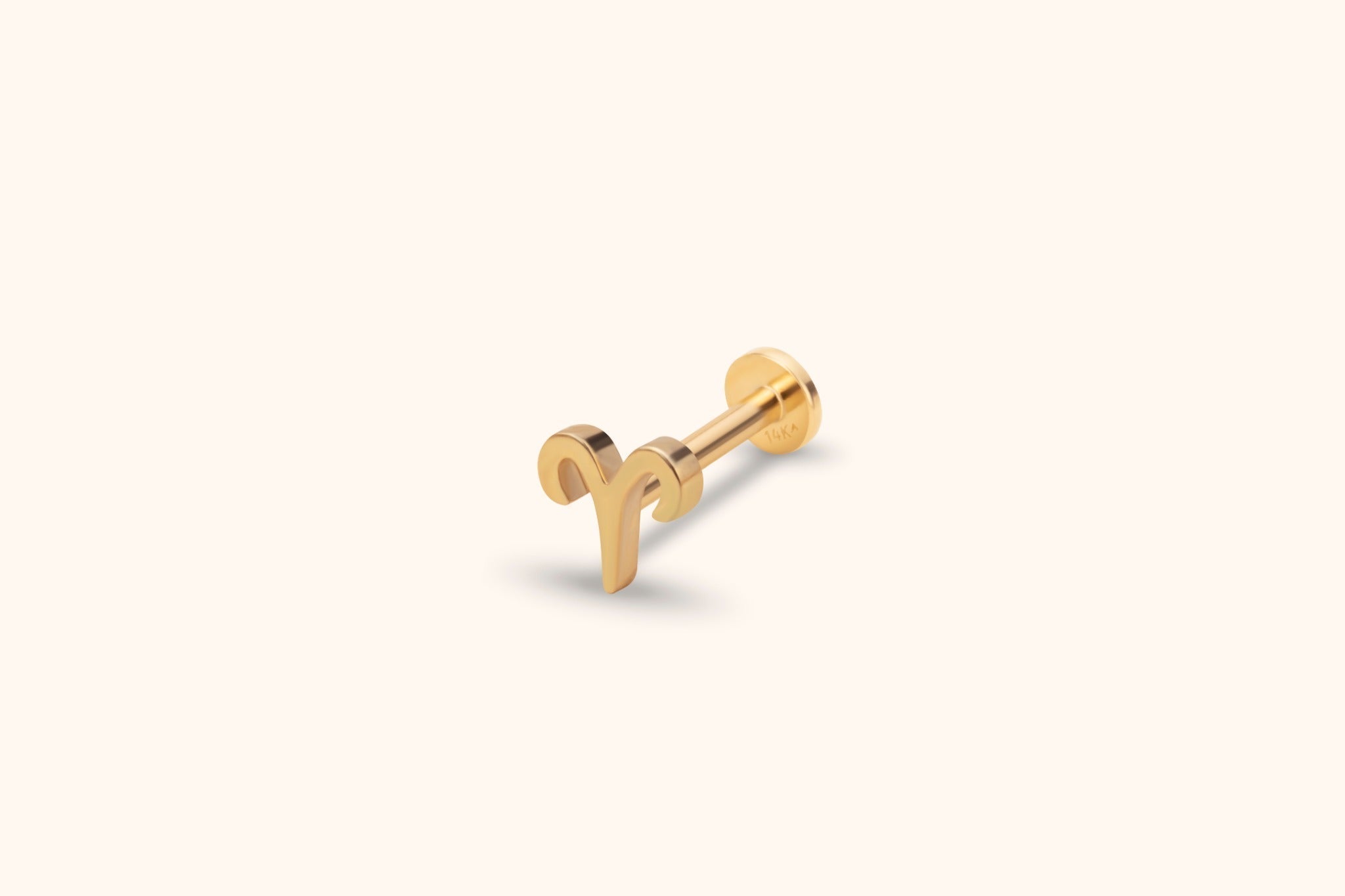 Gold-toned Aries symbol stud with a straight post and round flat back, shown at an angle on a pale cream background.