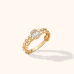 Gold-colored ring with an open geometric link band and rectangular clear stones bordered by round clear stones.