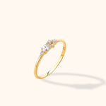 Slim gold-colored ring with an oval clear stone and four smaller round clear stones, shown at an angle on a pale background.