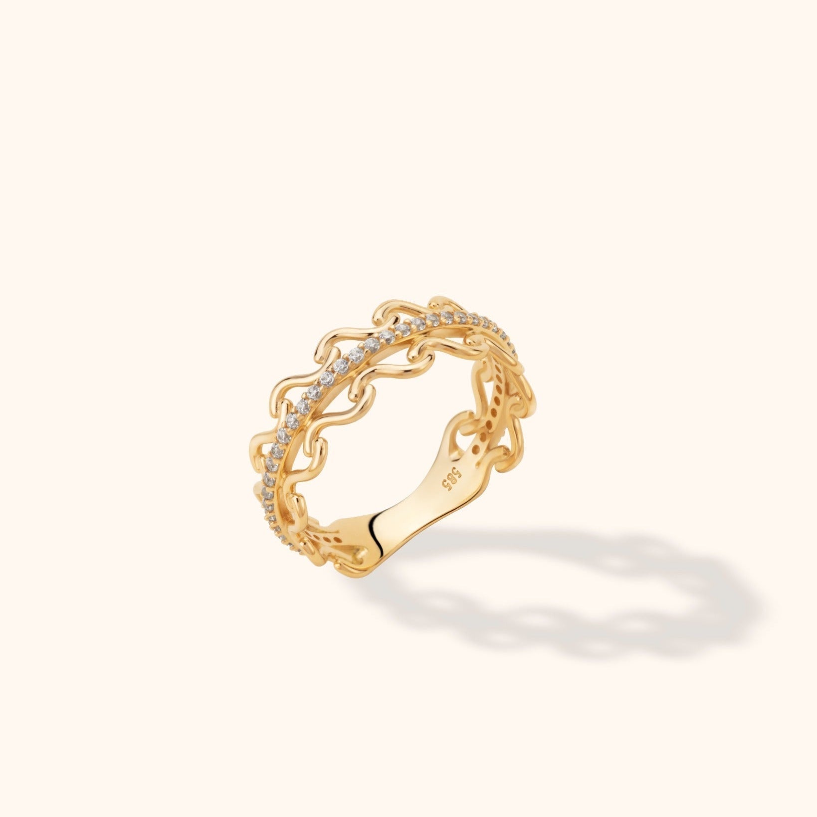 Gold-toned ring with open, wavy chain-link edges and a curved row of small clear stones, shown at an angle on a cream background.