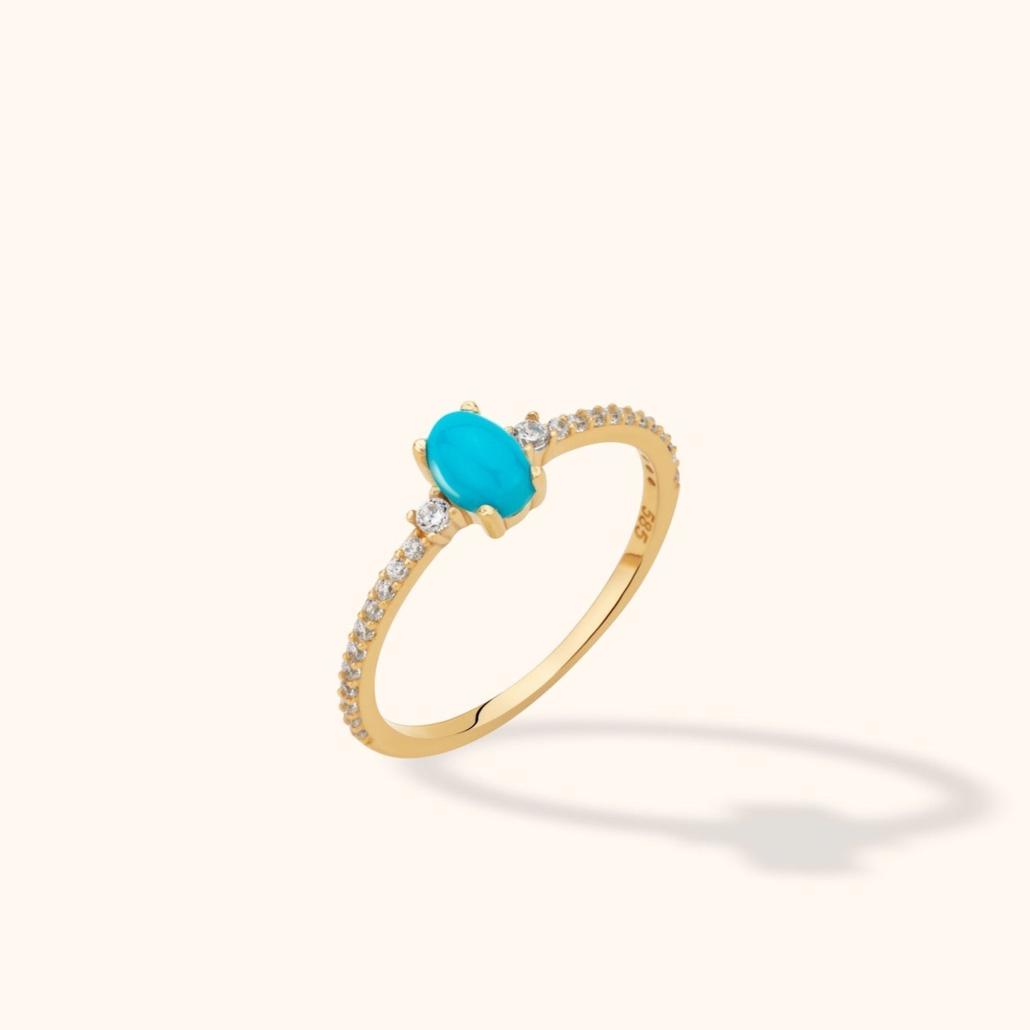 Gold-colored ring with an oval turquoise-blue center stone and small clear stones along a slim band, shown at an angle.