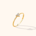 Slim gold-colored ring with three round clear stones in a triangular cluster, shown at an angle on a cream background.