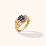 Gold-toned ring with a wide, ridged band, three rows of square blue stones and small clear accents, shown at an angle.