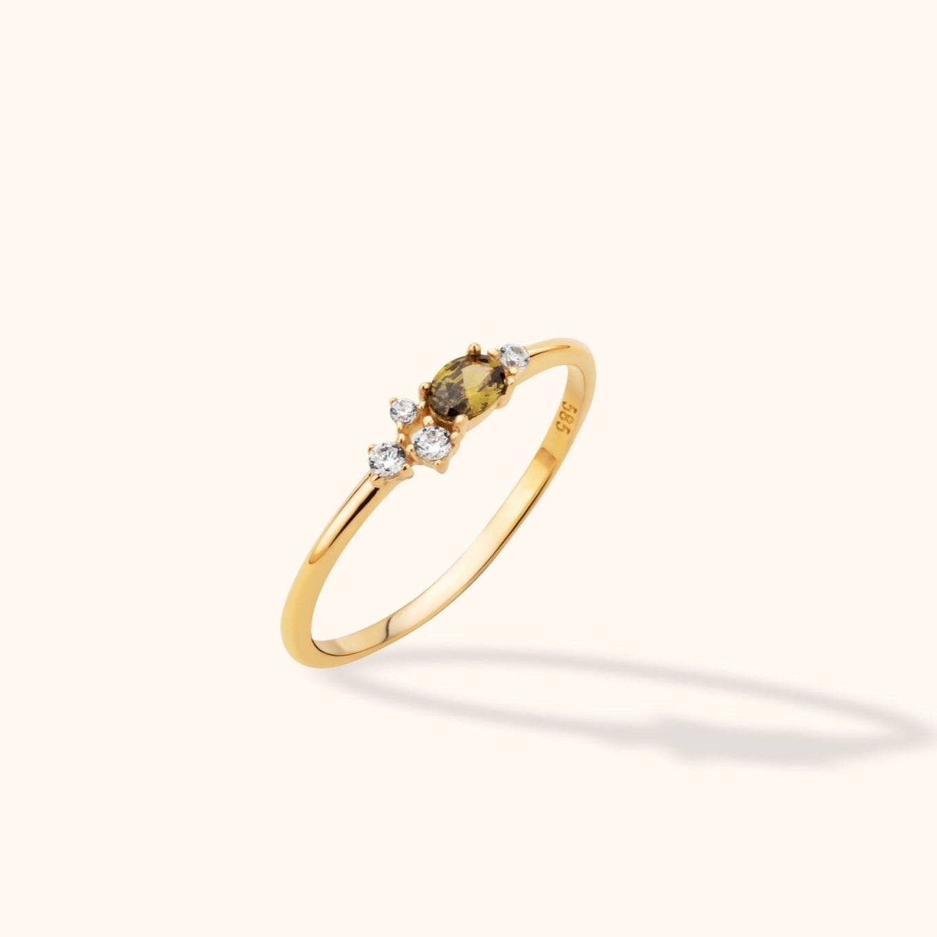Slim gold-toned ring with an oval olive-brown stone and four small clear accent stones, shown at an angle on a cream background.