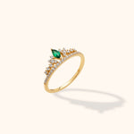 Gold-toned tiara-style ring with a marquise-shaped green stone and small clear stones, shown at an angle on a cream background.