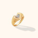 Polished gold-tone signet ring with a broad, tapered band and a heart filled with small clear stones, shown at an angle.