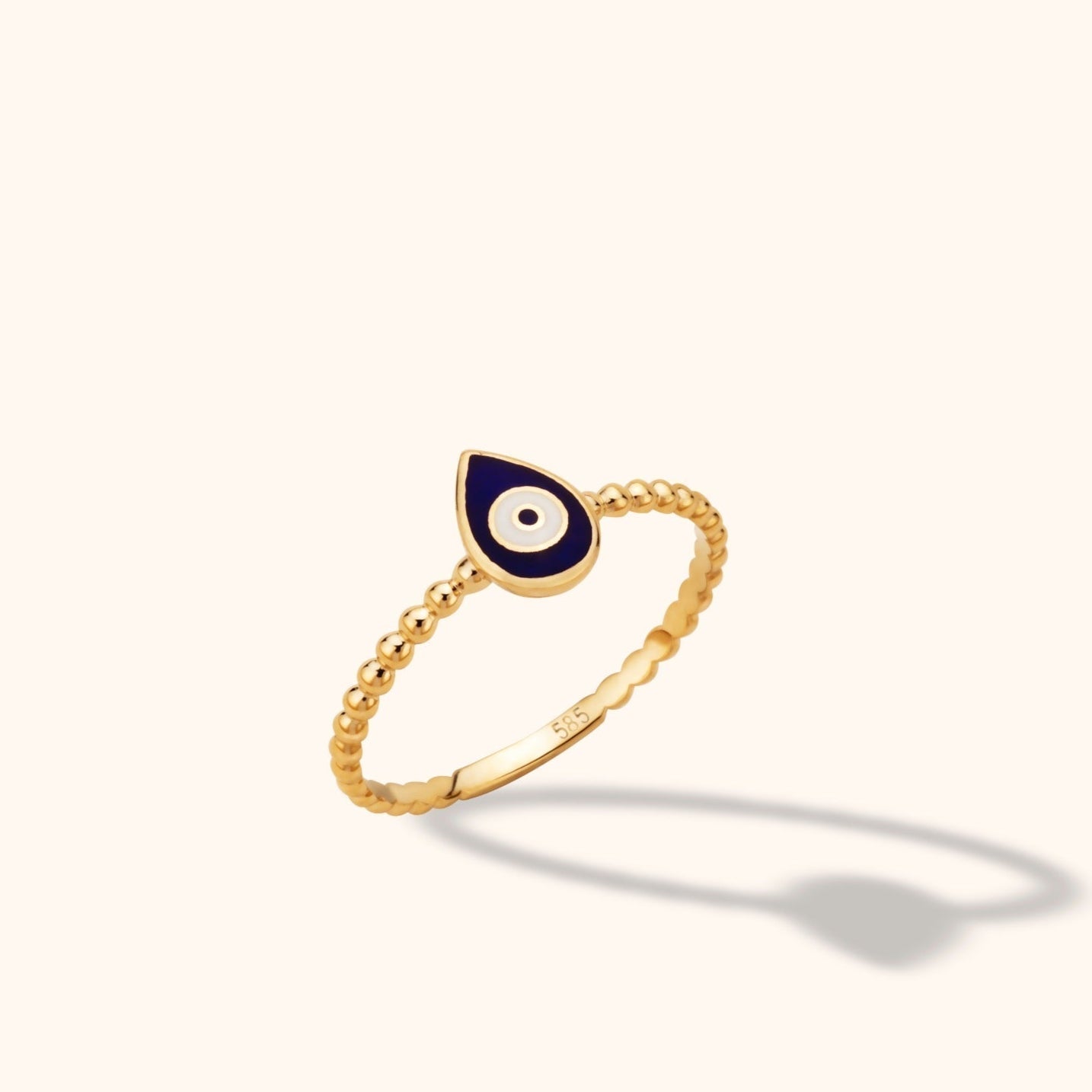 Gold-toned ring with a beaded band and a navy blue teardrop face featuring a white circular eye motif.