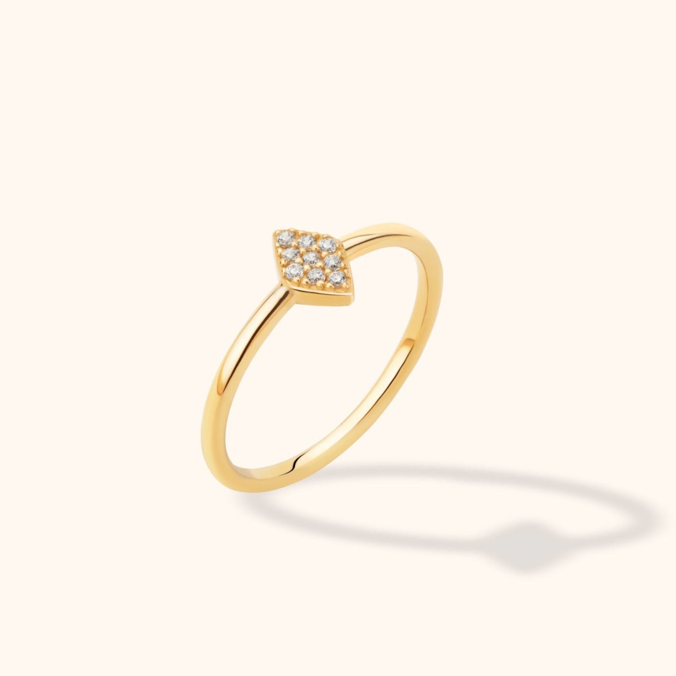 Slim gold-toned ring with a marquise-shaped cluster of small clear stones, shown at an angle on a cream background.