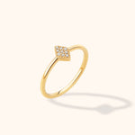 Slim gold-toned ring with a marquise-shaped cluster of small clear stones, shown at an angle on a cream background.