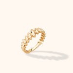 Polished gold-colored ring with repeating raised oval shapes and scalloped edges, tilted against a cream background.