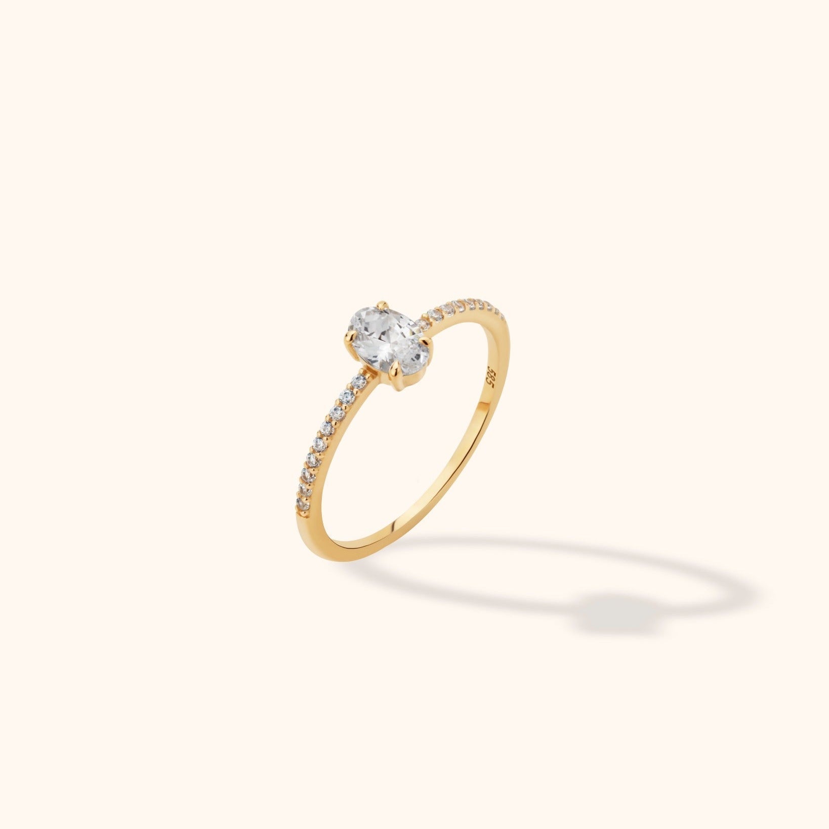 Gold-colored ring with an oval clear center stone in a prong setting and small clear stones along a slim band, shown at an angle.