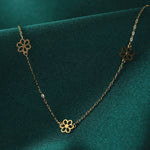 Gold-tone necklace with a fine oval-link chain and three openwork flower motifs, draped over dark green fabric.